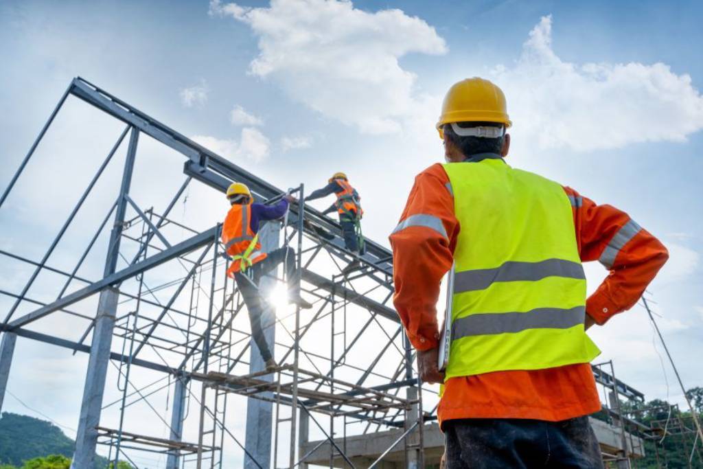 Construction workers building a metal framework under a clear sky.