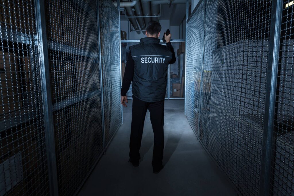 A security guard patrols a dimly lit corridor with metal fencing.